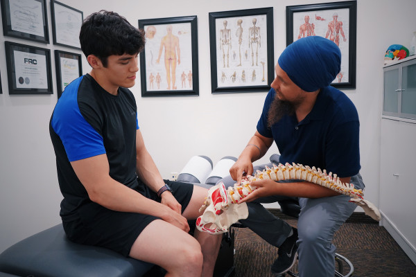 A doctor explaining a diagnosis to a patient using a spine model in a clinic setting