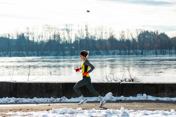 A woman runs along a frozen river in winter, staying active through the colder months.