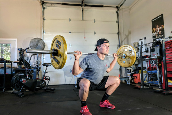 A man performing a barbell back squat in a gym, demonstrating force moving through the whole body