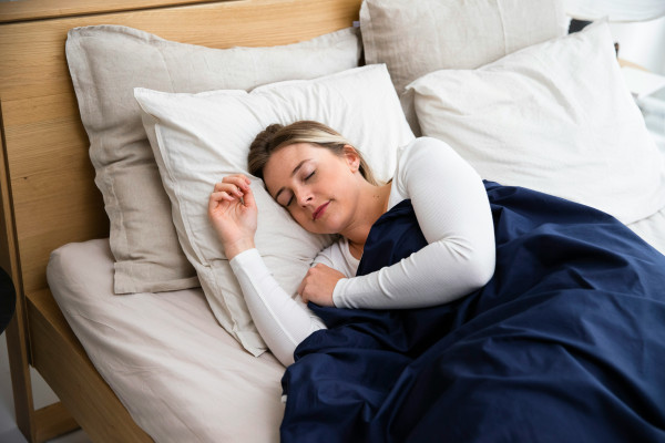 A woman sleeping peacefully in bed under a blue blanket.