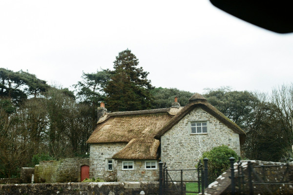 A stone cottage with a thatched roof, surrounded by trees in the English countryside.