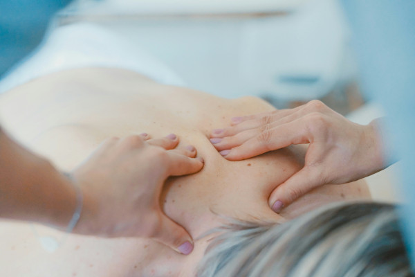 A therapist's hands applying gentle pressure to a person's upper back during a hands-on treatment.