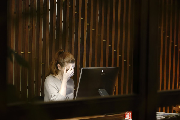 Woman sitting at a laptop with her hand pressed to her head, showing signs of tension and headache discomfort