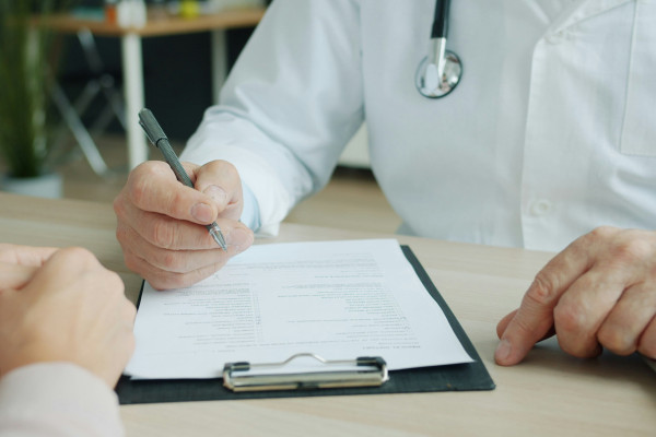 A clinician writing notes on a patient's chart during an appointment, reflecting the shared record that keeps treatment consistent between therapists