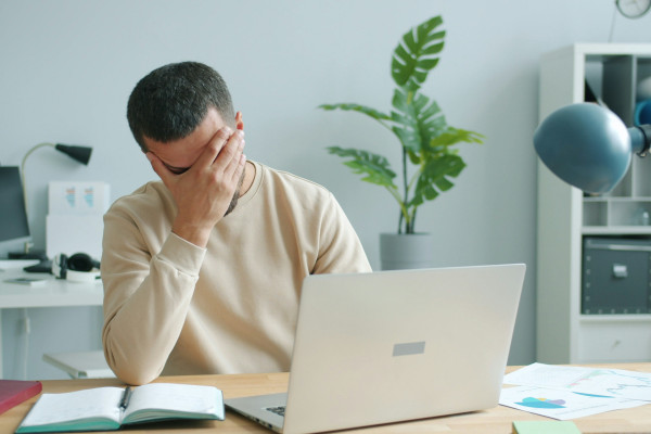 Man at a laptop rubbing his eyes and forehead in exhaustion, showing signs of work-related stress