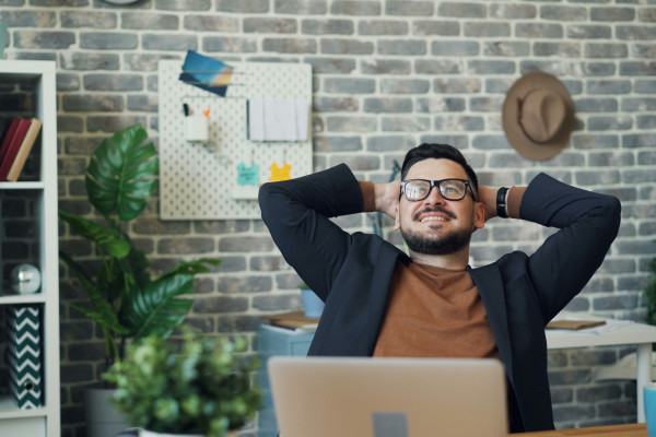A man sitting at a desk with his hands behind his head, taking a moment to stretch and pause.