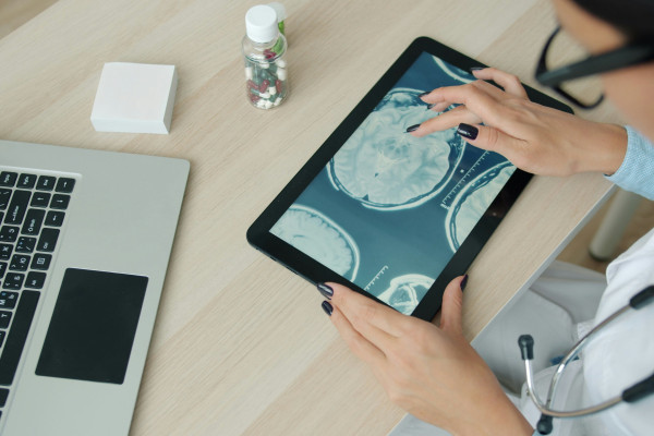 A medical professional studying a brain scan on a tablet at a desk.